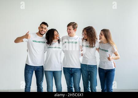 Young multiracial volunteers embracing and having fun over light studio wall, smiling and posing Stock Photo
