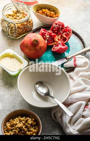 Yogurt, wholegrain granola, raisins, walnuts and pomegranate seeds on a table ready for breakfast Stock Photo