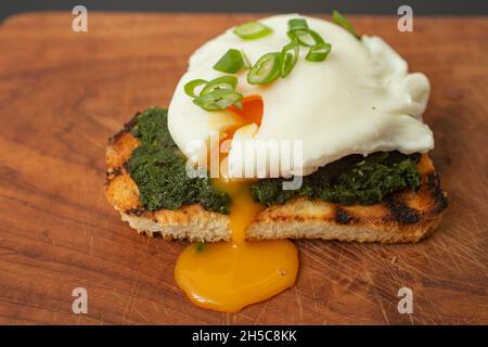 Selective focus close up , of a poached egg on a slice of toasted bread with spinach and spring onion, on the wooden table Stock Photo