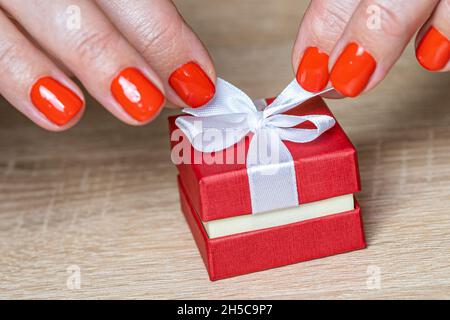 Hands tying ribbon on red gift box, top view. Stock Photo