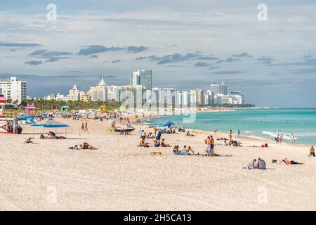 Miami Beach, USA - January 17, 2021: Many people at South Beach sand with buildings cityscape of coastline and beautiful blue turquoise water in Miami Stock Photo