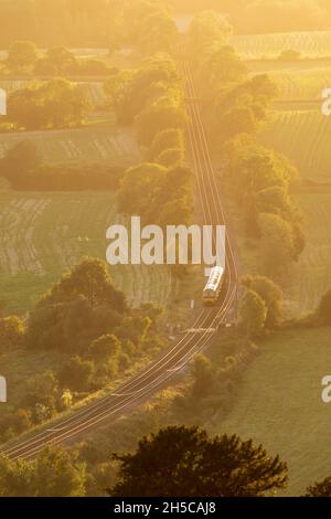 Train travelling through English countryside, Surrey, evening light, high viewpoint, North Downs Line. Sunlight shining on rails Stock Photo