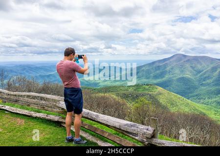 Devil's Knob overlook with man standing photographing taking picture of mountain view by wooden rustic countryside fence at Wintergreen resort town by Stock Photo