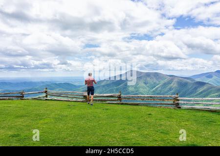 Devil's Knob Overlook with young man walking looking at view on meadow by wooden rustic countryside fence at Wintergreen resort town by Blue Ridge par Stock Photo