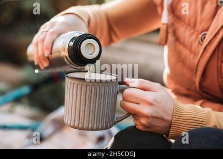 Close-up of female hands pouring tea from a metal vacuum bottle to the mug Stock Photo