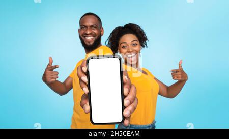 Check this out, cellphone display mockup. Cheery black couple pointing at cellphone with empty screen on blue background Stock Photo