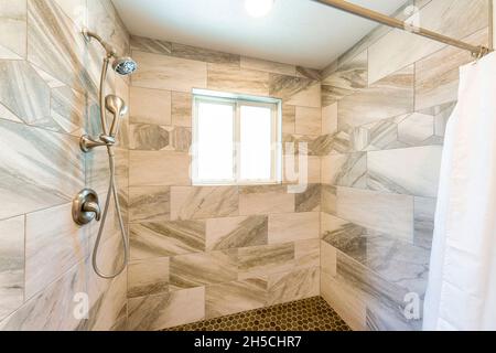 Shower stall interior with marble tile surround and small hexagon pattern tile flooring Stock Photo