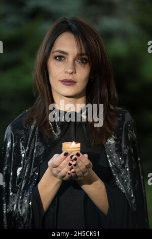 Portrait of an attractive young woman in a black dress with a cape. In the hands of a burning candle. A girl with dark hair and brown green eyes and m Stock Photo