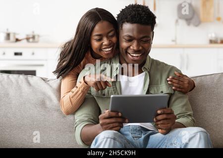 Cheerful african american couple having fun at home, using pad Stock Photo