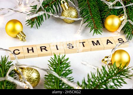 Wooden Christmas text with green fir tree branches, golden baubles and lights as Xmas seasonal decorations on white background for greeting cards. Stock Photo