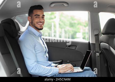 Handsome arabic entrepreneur sitting at auto, using laptop, mockup Stock Photo