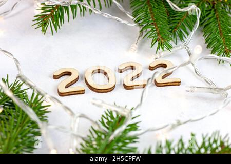 Wooden numbers 2022 silhouette with green fir tree branches and lights on light background. New Year beginning congratulations and planning concept. Stock Photo