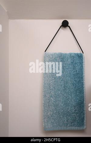 Blue and white hand towel hanging on a black metal hook, isoalted against a white wall. Stock Photo