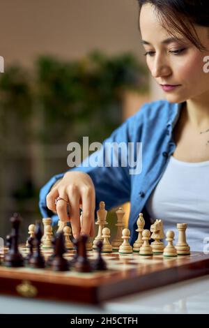 Young woman moving chess pieces on the board while playing chess game at home alone Stock Photo