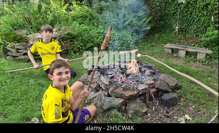 two brothers in Borussia Dortmund jerseys baking stick bread over an open fireplace , Germany, North Rhine-Westphalia, Ruhr Area, Dortmund Stock Photo
