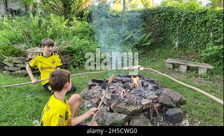 two boys in Borussia Dortmund jerseys baking stick bread over an open fireplace , Germany, North Rhine-Westphalia, Ruhr Area, Dortmund Stock Photo