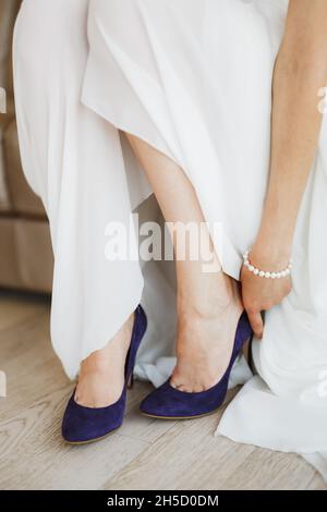 Bride in a white dress with a pearl bracelet on her arm wears blue high-heeled shoes on her feet. Close-up Stock Photo