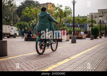 Lima, Peru - 12.02.2019: Peruvian person wearing a green jaket riding a bicycle on a cycling track Stock Photo