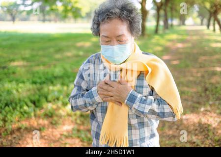 Senior woman wearing medical mask and  clutching her chest in pain Stock Photo