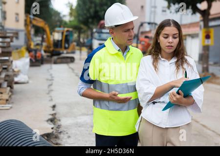 Man engineer and a young woman discuss a construction project while , taking important notes Stock Photo