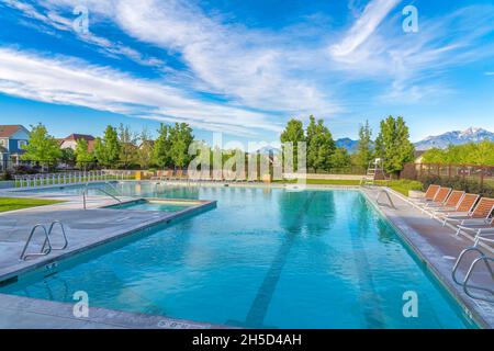 Large public pool surrounded by lounge chairs and wire fence at Daybreak, Utah Stock Photo