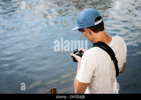 Young Adult Photographer Standing by the Water Holding a Camera Stock Photo