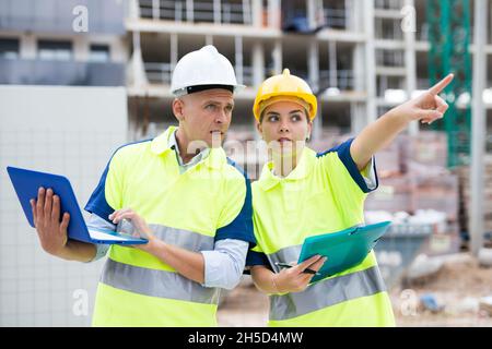 Male and female european builders talking about their work while standing in construction plant. Stock Photo