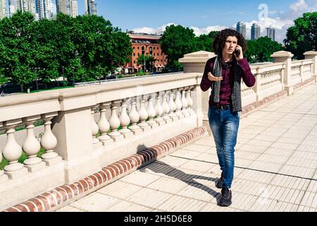 A portrait of a serious curly-haired young latin man walking down a sidewalk Stock Photo