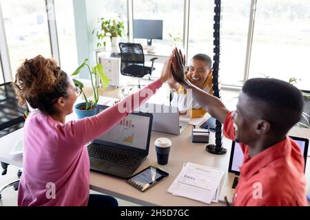 Cheerful multiracial business colleagues giving high-five at desk in creative office Stock Photo