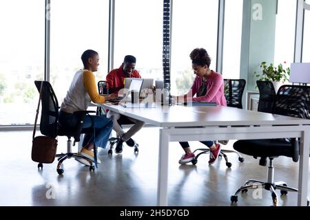 Multiracial business colleagues in casuals smiling while working on laptops in creative office Stock Photo