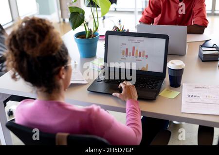 Businesswoman in casuals analyzing chart on laptop at desk in creative office Stock Photo