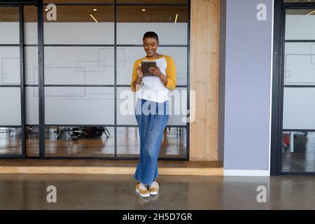 Smiling african american creative businesswoman in casuals using tablet pc while standing in office Stock Photo