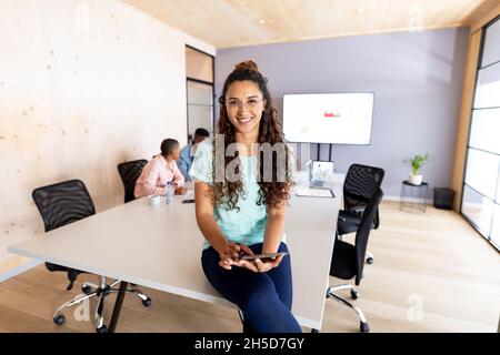 Portrait of smiling biracial businesswoman in casuals using tablet pc on conference table in office Stock Photo