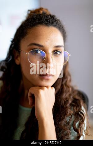 Close-up portrait of confident biracial businesswoman with hand on chin in eyeglasses at office Stock Photo