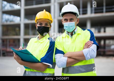 Two engineers in protective masks are discussing a construction plan Stock Photo