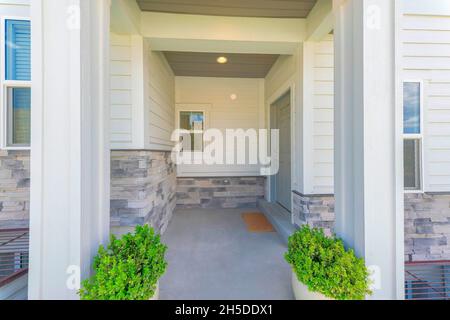 Entrance of a house with gray door on the side and two potted plants near the column posts Stock Photo