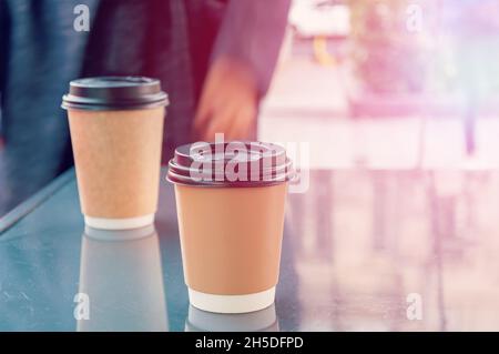 Two disposable cups of coffee are on a table near the cafe. Autumn, cold weather and warming drinks. Stock Photo