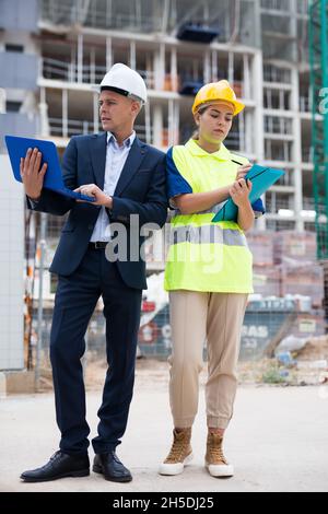 Man engineer standing on a construction site with a young woman worker monitors the construction plan on a laptop Stock Photo
