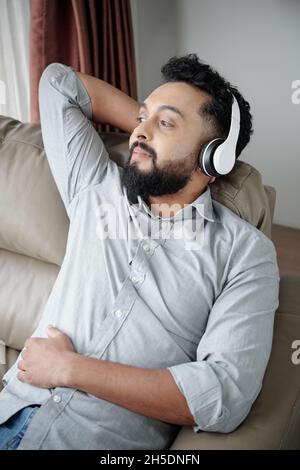 Smiling bearded man listening to music in headphone and relaxing in armchair Stock Photo