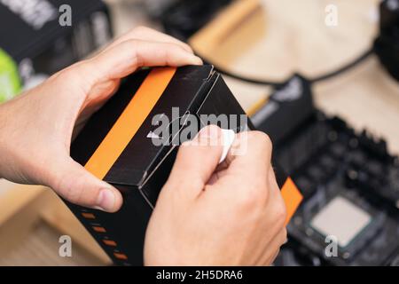 man opening black and orange box consisting of some electronic components on wooden table. Broken computer. Future programmer. Stock Photo