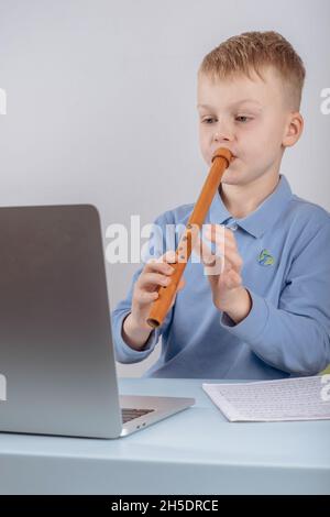 Boy learning to play the flute watching online course on laptop while practicing at home. Online training, online classes. High quality photo Stock Photo