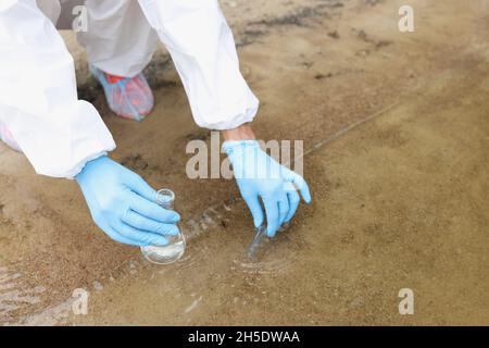 Scientist in protective suit and gloves taking test tube from lake closeup Stock Photo