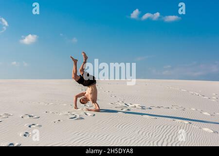 Young sporty man want doing acrobatic exercises on the sand near river Stock Photo