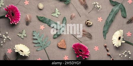 Jungle floral flat lay on linen textile. Bold tropical plant mix with dark red, burgundy and white gerbera flowers, feathers, quail eggs. Springtime Stock Photo