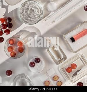 Cosmetic skincare background with red grapes. Abstract white flat lay cosmetic laboratory background with chemical glassware. Herbal remedies in Stock Photo