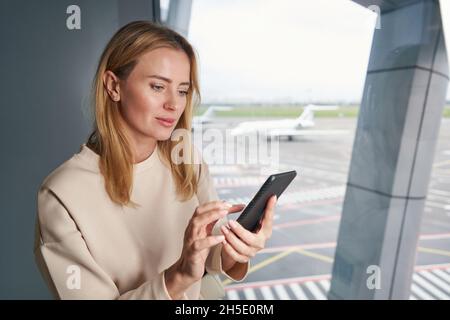 Focused Caucasian young traveler using her cellphone indoors Stock Photo
