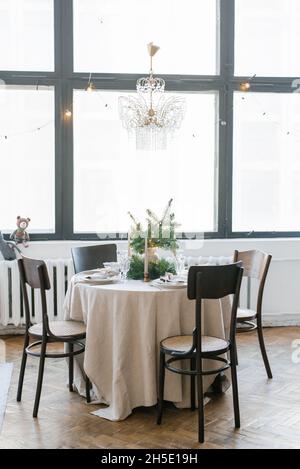 A dining table with wooden chairs, decorated and served for Christmas dinner against the background of a large window in the house, a crystal vintage Stock Photo