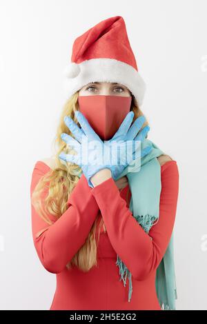 Lady santa in red clothing, protective mask and blue latex gloves, holds crossed hands near her face Stock Photo