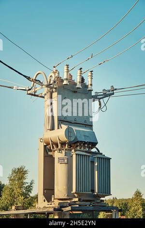 Old grey power transformer with ceramic insulators and connected cables under clear blue sky at sunset light close view Stock Photo