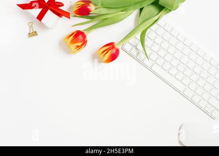 Feminine composition of women's work space, gifts for Mother's Day and Valentine's Day. Gift with a red ribbon and a bouquet of tulip flowers, keyboar Stock Photo